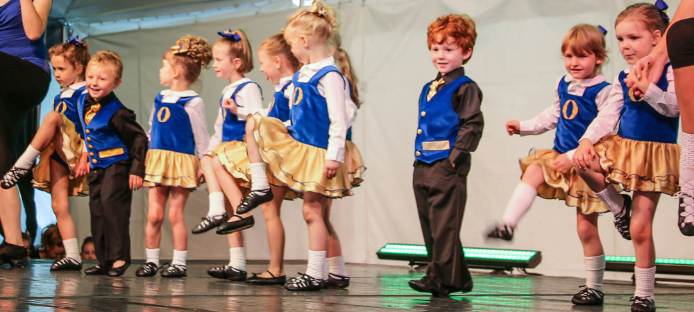 Young girls and boys on stage showing their Irish steps. Grinning.